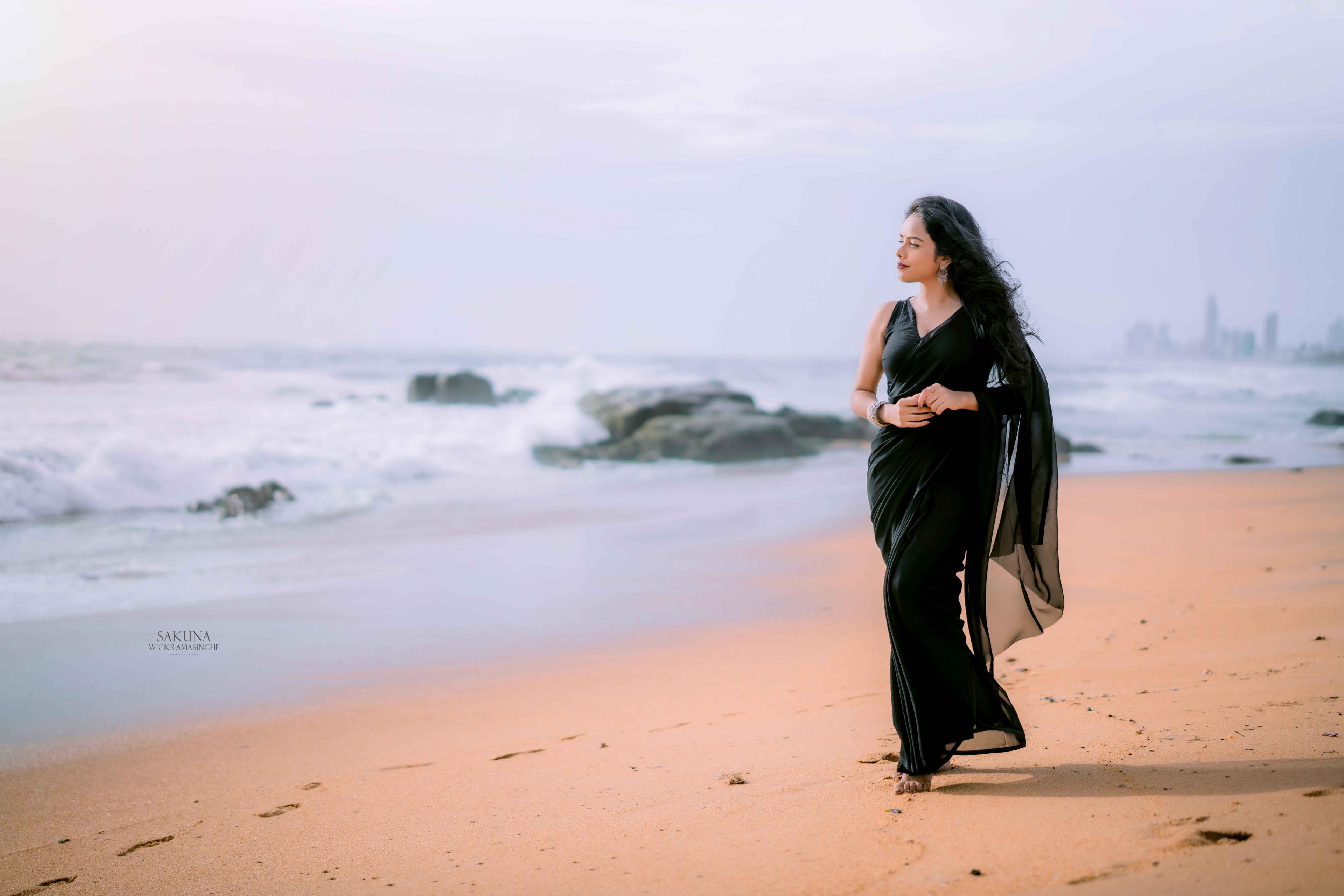 Model in a black saree walking on a golden beach at sunset