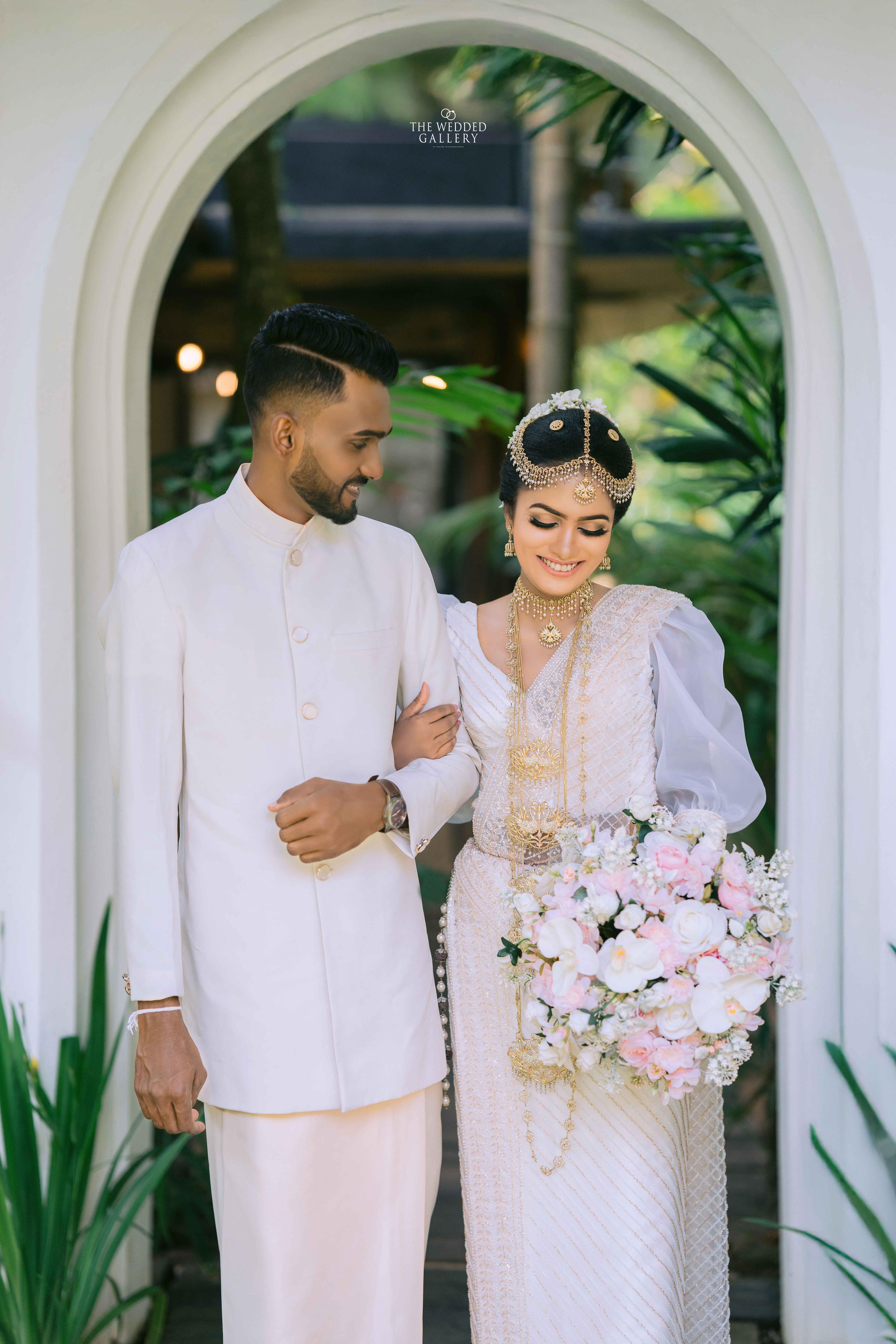 Bride and groom walking through a white arched doorway with a pastel bouquet
