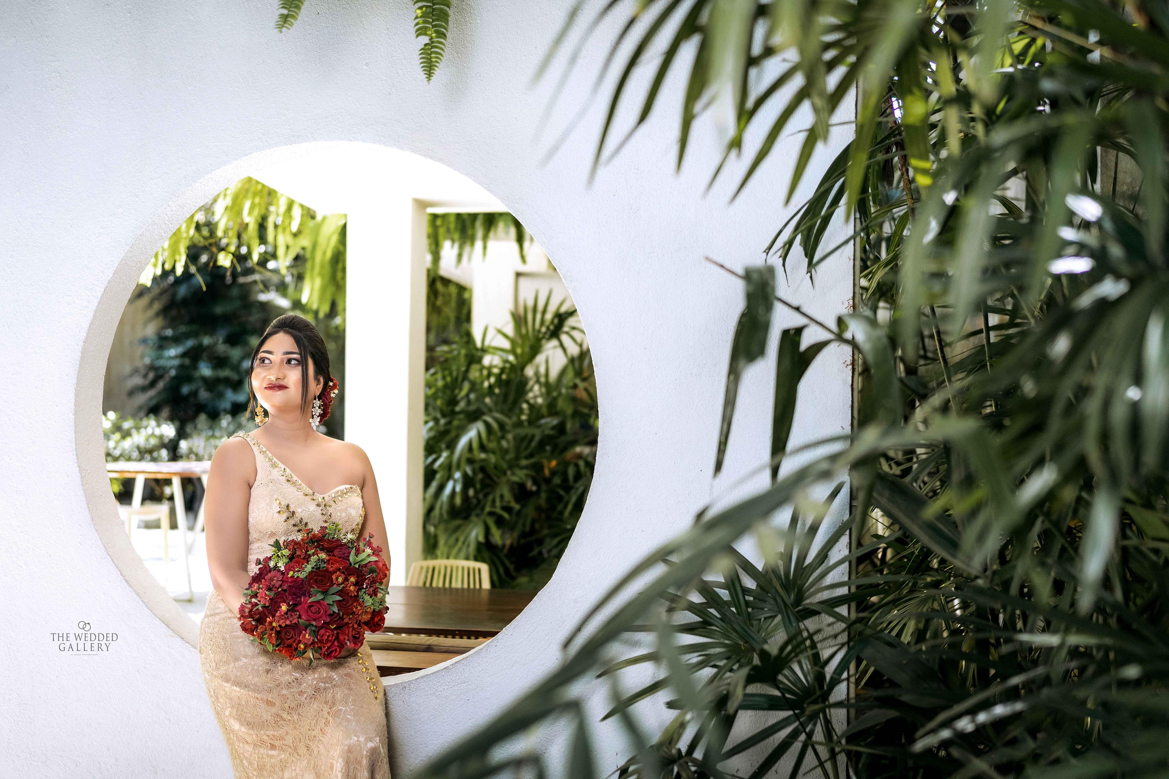 Bride in a gold gown holding red roses in front of a round moon window